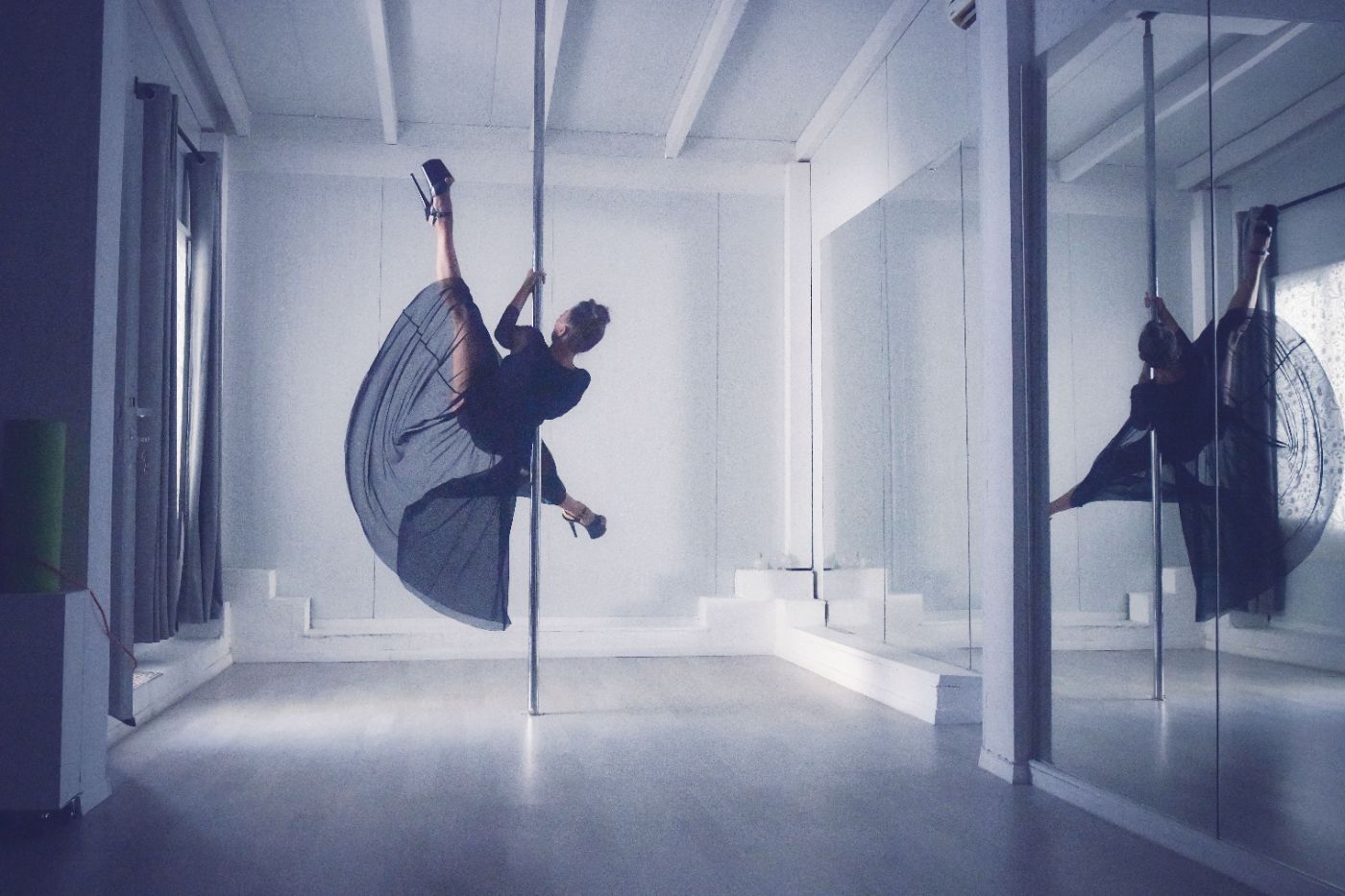 Member mid-spin on a pole, reflected in the studio mirrors